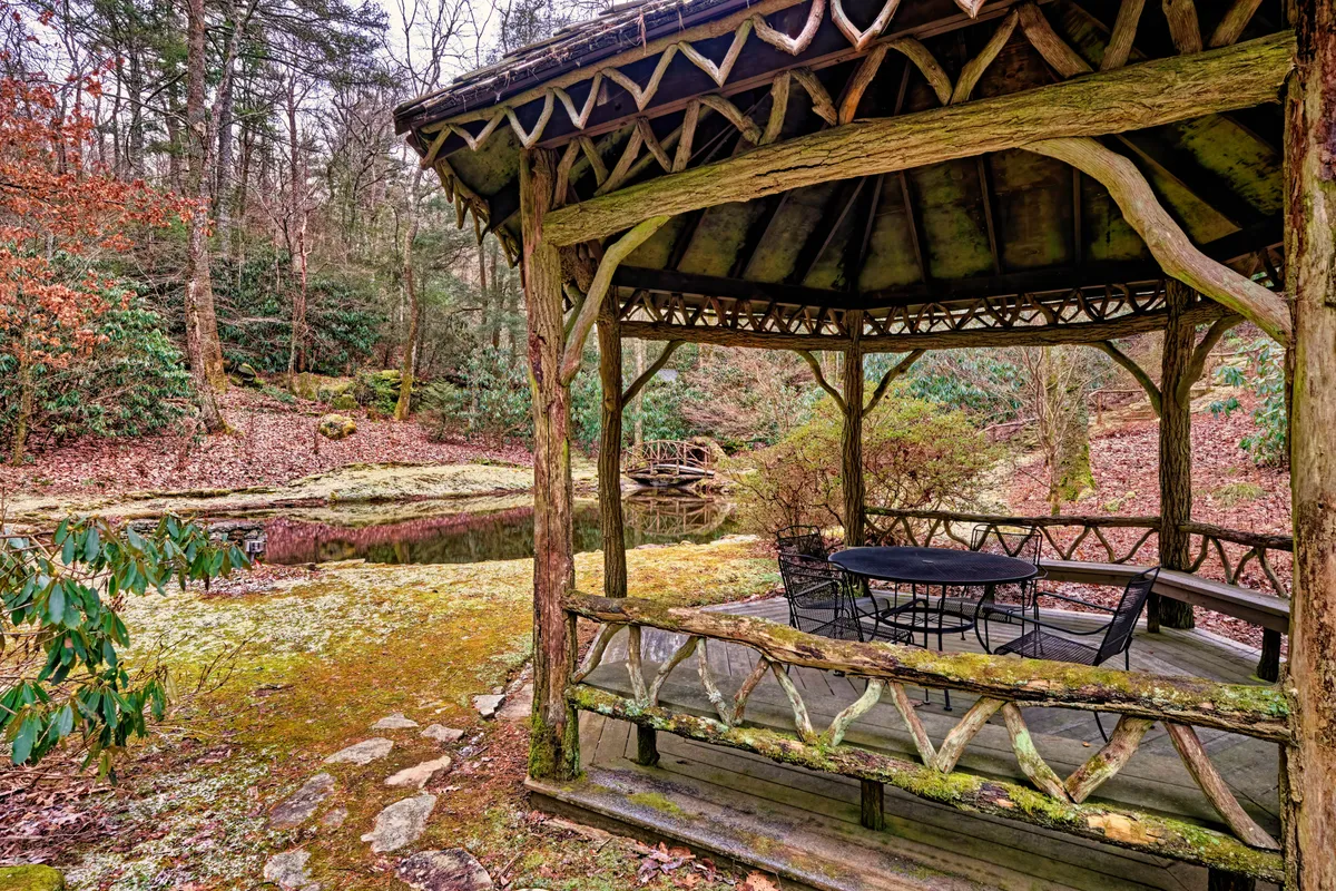 This image features a tranquil gazebo sitting by a peaceful pond, with a wooden railing enclosing the space. The natural greenery and water create an inviting atmosphere for relaxation, reading, or quiet reflection.