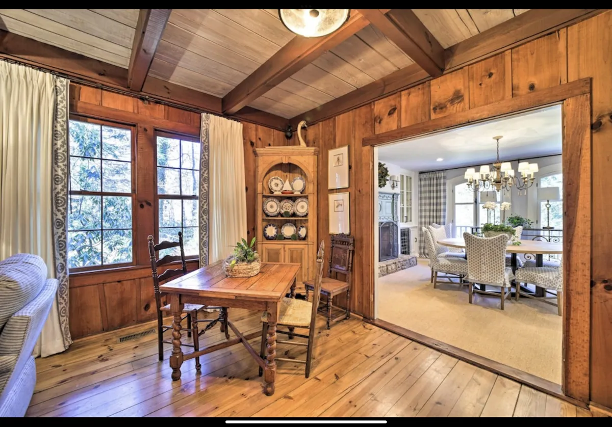 A view of a wooden table set for gathering, with a display cabinet and a dining area visible beyond. The space is designed for family meals, intimate celebrations, or spirited game nights, featuring warm lighting and inviting decor.