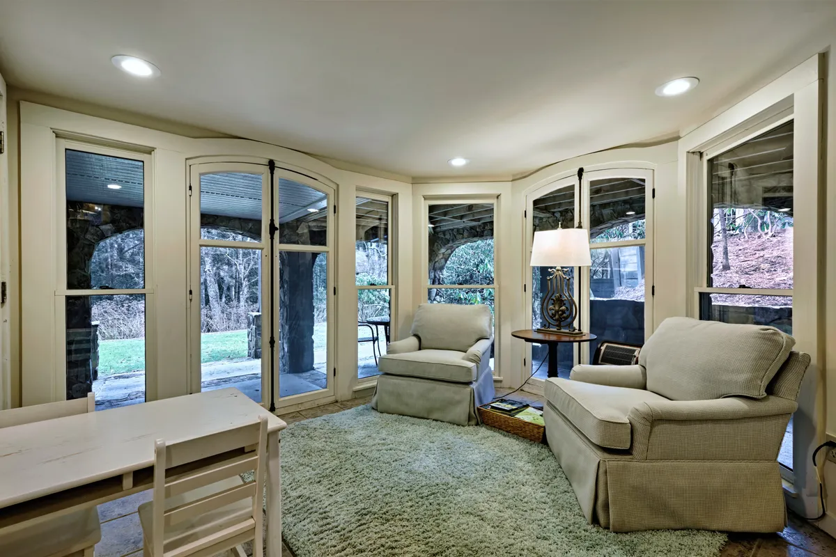 A cozy seating area with two comfortable chairs, a table lamp, and a large window offering expansive views of the natural setting outside. The room is warmly decorated and filled with soft, inviting light.