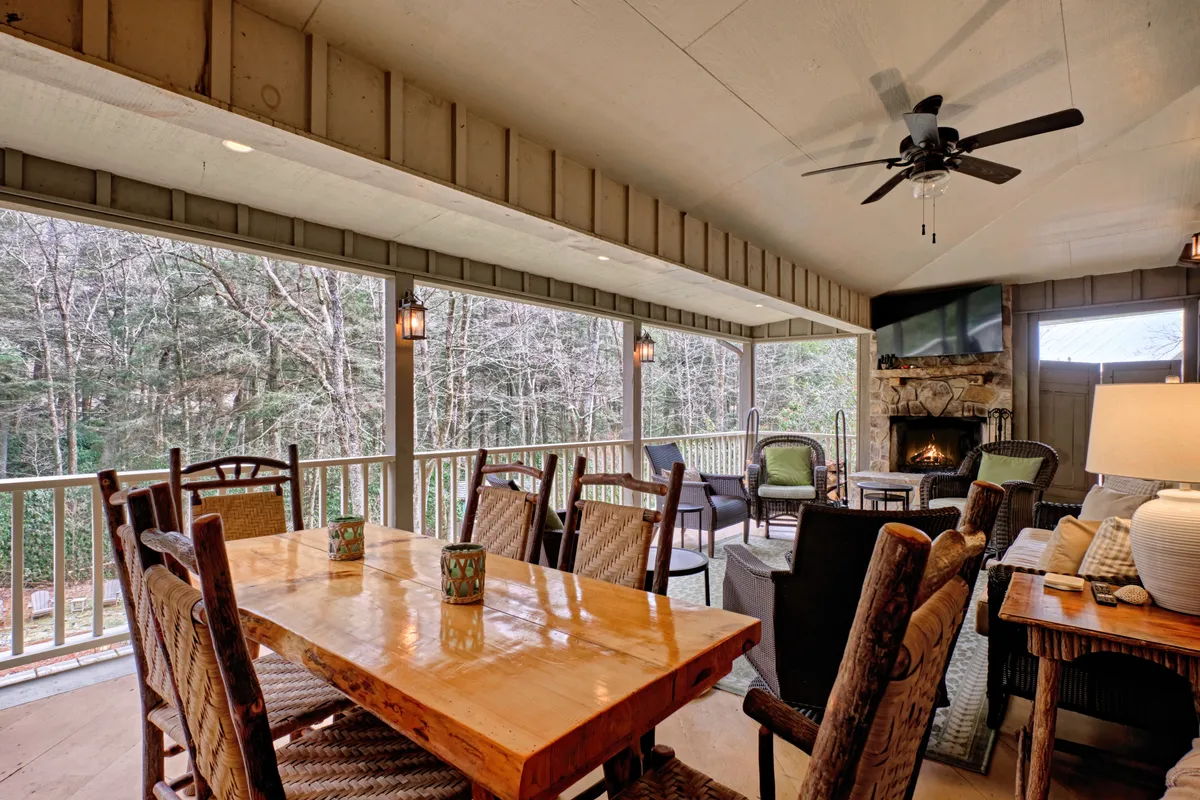 This interior showcases an expansive wooden dining table seamlessly adjoining a comfortable seating area and fireplace, all set against large windows that frame serene natural views. The room feels bright and open, ideal for celebratory feasts and shared meals.
