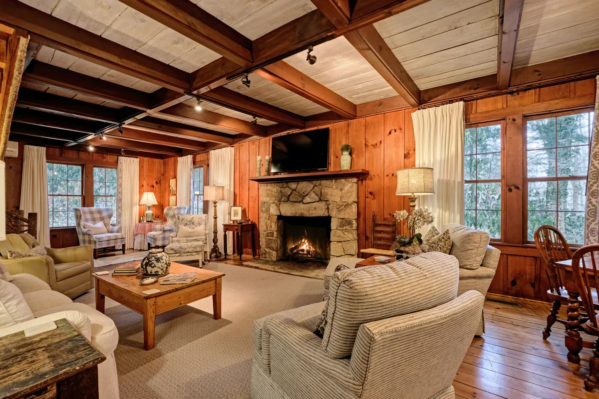 A warm, comfortable interior scene featuring a fireplace, plush seating, exposed wooden beams, and expansive windows. The space is ideal for reading by the fire, socializing, or playing board games, exuding a sense of togetherness and comfort.